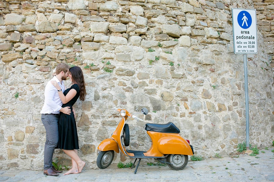 Couple share a fun embrace beside an orange Vespa in Italy